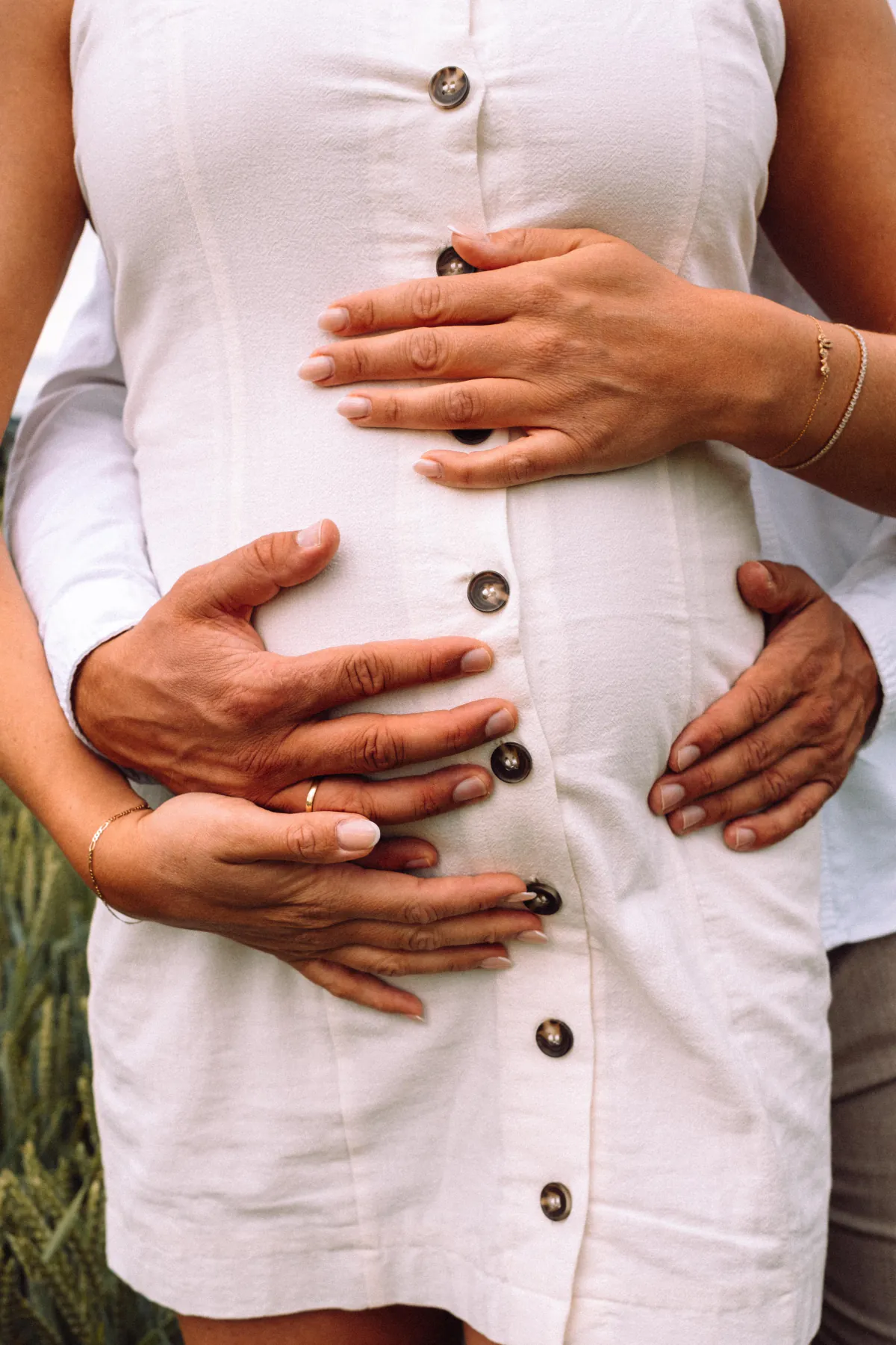 Hände auf dem Babybauch einer Frau im weißen Kleid